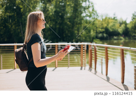Solo tourist Woman with paper map and smartphone stands on a bridge into a river. Person in sport clothes walking on nature background. Wanderlust travel concept, atmospheric moment, earth day 116124415