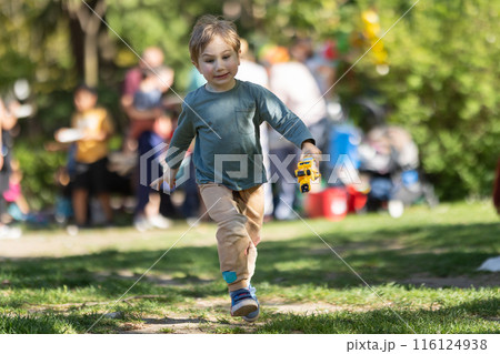 A young boy is running through a park with a toy bus in his hand A young boy is running through a park with a toy bus in his hand 116124938