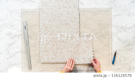 In the process of mounting peel and stick mosaic tiles onto a foam board, perfect for enhancing a food photography studio's aesthetic. 116128570