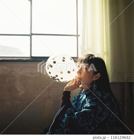 大きい窓からの光と風船を膨らませる女性 116129682