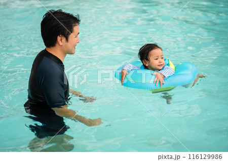 happy father with toddler baby girl playing in an inflatable ring in swimming pool 116129986