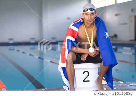 Male athlete swimmer wrapped in Australian flag sitting on podium with gold medal 116130856
