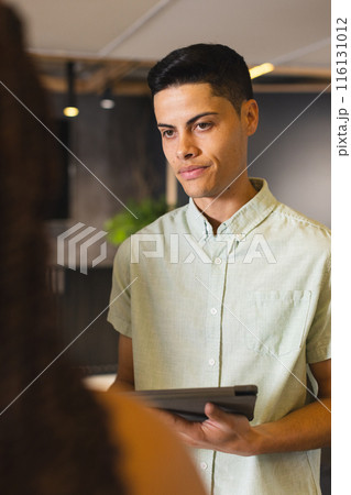 A biracial man holding tablet, talking to someone off-camera in a modern business office 116131012
