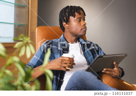 African American man holding coffee, looking at tablet in a modern business office 116131037