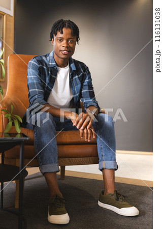 African American man sitting in chair in a modern business office, wearing casual clothes African American man sitting in chair in a modern business office, wearing casual clothes 116131038