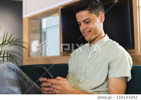 A young biracial man with short dark hair is looking at his smartphone in a modern business office 116131042