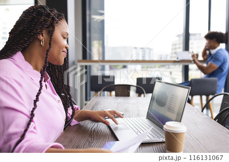 A young biracial woman with braided hair is working on a laptop in a modern business office 116131067