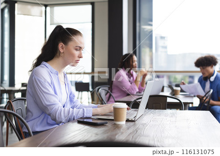 Caucasian woman typing on laptop in a modern business office, biracial woman and man talking 116131075