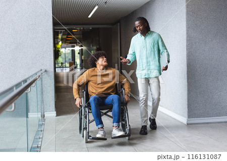 African American man pushing wheelchair of biracial man, both talking in a modern business office African American man pushing wheelchair of biracial man, both talking in a modern business office 116131087
