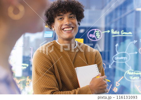 A young biracial male holding notepad, discussing ideas in a modern business office 116131093