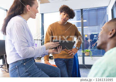 Diverse team discussing over tablet, standing in office 116131095