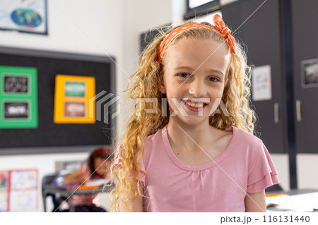 In school, young Caucasian girl with curly blonde hair is smiling in a classroom 116131440