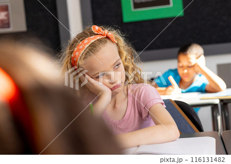 In school, young Caucasian girl with curly blonde hair looks thoughtful in the classroom 116131482