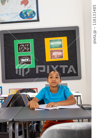In school, young biracial boy sitting at a desk in a classroom, looking forward In school, young biracial boy sitting at a desk in a classroom, looking forward 116131485