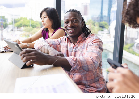 Diverse group of young adults working together in a modern business office, smiling at camera Diverse group of young adults working together in a modern business office, smiling at camera 116131520
