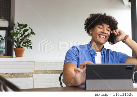 A young biracial man wearing a blue shirt is talking on the phone in a modern business office A young biracial man wearing a blue shirt is talking on the phone in a modern business office 116131526