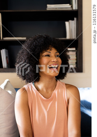 Biracial young woman laughing, sitting on couch at home Biracial young woman laughing, sitting on couch at home 116131579