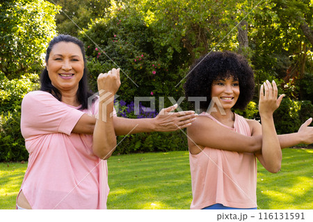Mature biracial woman and young biracial woman exercising in garden at home 116131591
