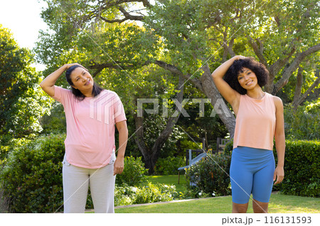 Mature biracial woman and young biracial woman stretching in park at home 116131593