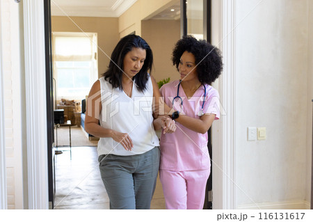Mature biracial woman walking with young biracial nurse, both looking down at home Mature biracial woman walking with young biracial nurse, both looking down at home 116131617
