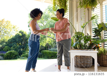 Biracial mother and adult daughter are drinking coffee outside at home 116131635
