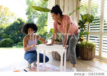 Biracial mother and adult daughter are painting furniture outside at home as an upcycling project 116131636