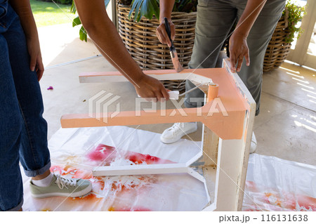 Biracial mother and adult daughter are painting a table together at home as an upcycling project 116131638