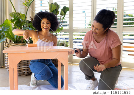 Biracial mother and adult daughter painting furniture together at home in an upcycling project 116131653