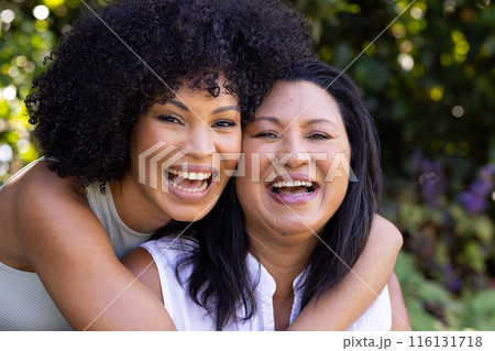 Biracial mother and adult daughter are laughing together outdoors at home in the garden 116131718