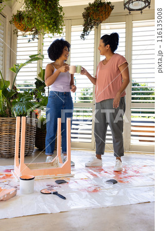 Biracial mother and adult adult daughter enjoying coffee during home painting and upcycling project 116135008