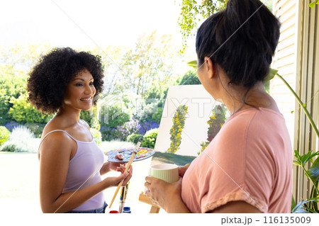 Mother and Daughter, mature biracial woman holding coffee mug watching young biracial woman painting Mother and Daughter, mature biracial woman holding coffee mug watching young biracial woman painting 116135009