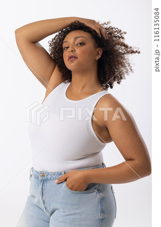 Biracial young female plus size model with curly brown hair posing confidently on white background, 116135084