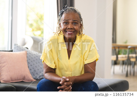 African American senior woman sitting at home, wearing a yellow shirt and jeans 116135734