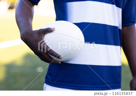 African American young male athlete on field outdoors holding a white rugby ball African American young male athlete on field outdoors holding a white rugby ball 116135837