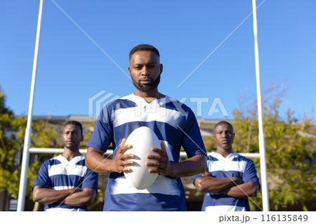 Three African American young male athletes holding a rugby ball, standing on field outdoors 116135849