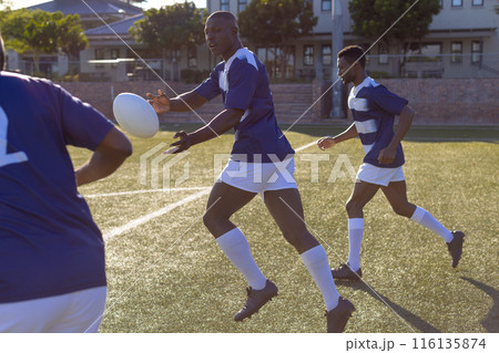 Three African American young male athletes are playing rugby on field outdoors 116135874