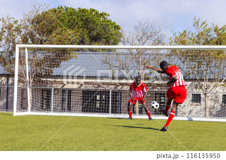 Two African American young male athletes are playing soccer on field outdoors, one kicking the ball Two African American young male athletes are playing soccer on field outdoors, one kicking the ball 116135950