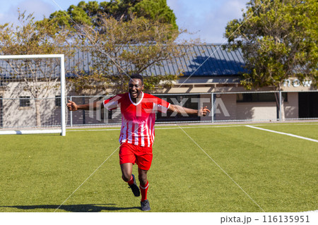 African American young male athlete wearing red and white soccer uniform running on field outdoors African American young male athlete wearing red and white soccer uniform running on field outdoors 116135951