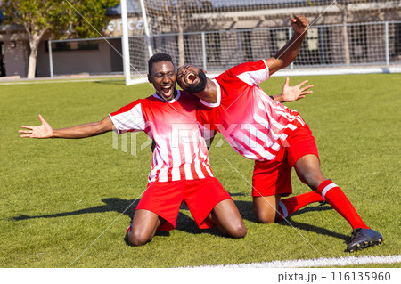 Two African American young male athletes are celebrating on a soccer field outdoors 116135960