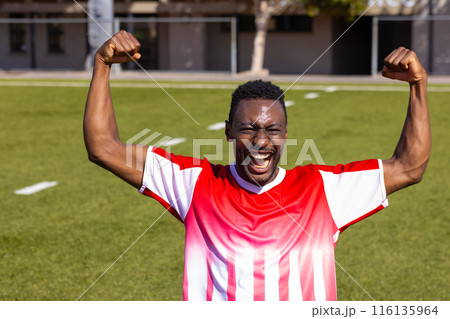 African American young male athlete celebrating on field outdoors, raising arms African American young male athlete celebrating on field outdoors, raising arms 116135964