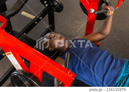 An African American young male athlete is training with a chest press machine in a gym 116135979