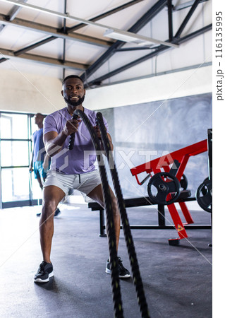 Two African American young male athletes are training with battle ropes in gym 116135995