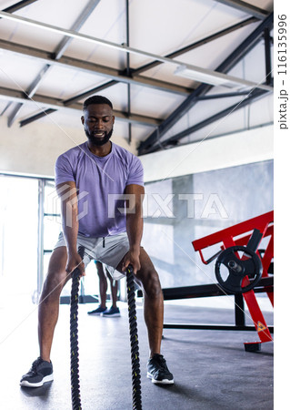 African American young male athlete training with heavy ropes in gym African American young male athlete training with heavy ropes in gym 116135996
