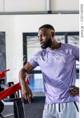 African American young male athlete leaning on gym equipment in gym, taking a break 116136000
