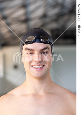 Caucasian young male swimmer smiling indoors, wearing goggles on his head Caucasian young male swimmer smiling indoors, wearing goggles on his head 116136029