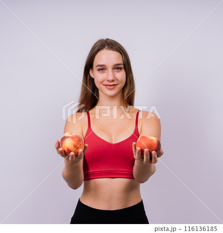 Happy cheerful young blond woman holding nectarines in hands over chest 116136185