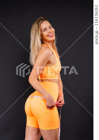 A weight loss and healthy lifestyle concept. Smiling slim woman measuring her waist with tape 116136261