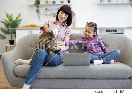 Mother and daughter relaxing on couch with cat and laptop 116136290