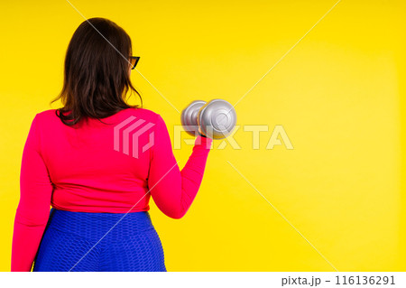 Sporty model with curvy figure with dumbbells. Dynamic movement. Motivation and healthy lifestyle Sporty model with curvy figure with dumbbells. Dynamic movement. Motivation and healthy lifestyle 116136291