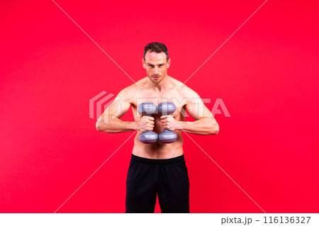 Adult muscular man smiling and screaming while working out hard with dumbbells. 116136327